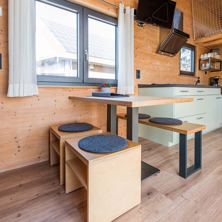 Essbereich mit Tisch und Bänken und im Hintergrund die Küche