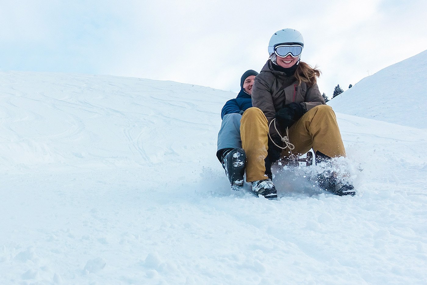 Zwei Personen auf dem Schlitten im Schnee, die den Berg herunter fahren