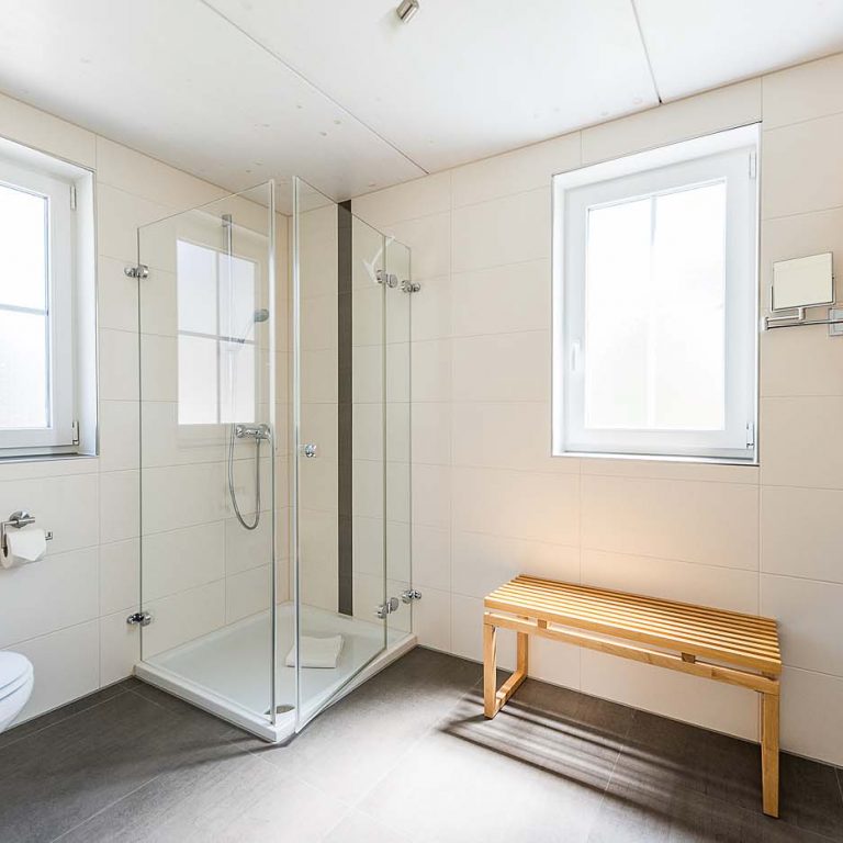 Dusche mit Spiegel, Duschkabine, Waschbecken und Sitzmöglichkeit